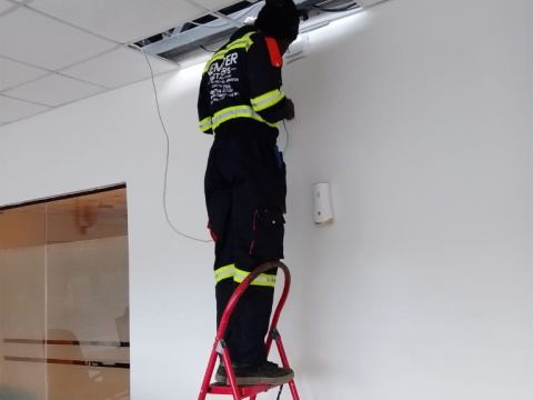 Nemster technician in branded uniform on a ladder routing cable through an office ceiling